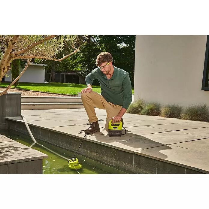 Ryobi ONE+ Bomba para aguas residuales - Capacidad de bombeo máx.: 4.200 l/h - Hombre usa una bomba de agua portátil Ryobi verde lima con su entrada en un estanque para limpiar.