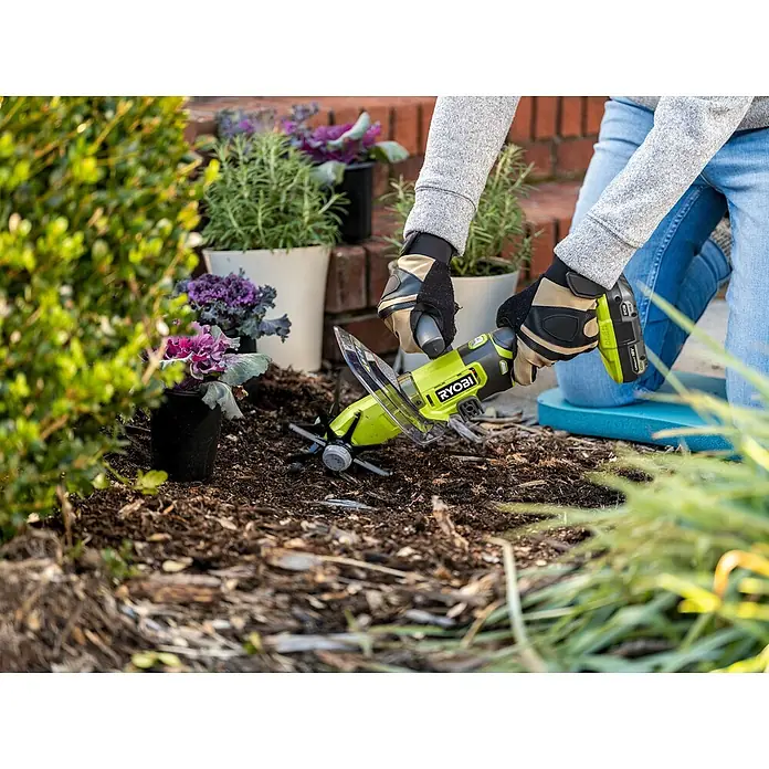 Ryobi ONE+ Akku-Bodenhacke RY18HCA-018 V, Ohne Akku - Eine Person benutzt einen Ryobi-Kultivator, um den Boden in einem Garten vorzubereiten, der mit Pflanzen und Blumen geschmückt ist.