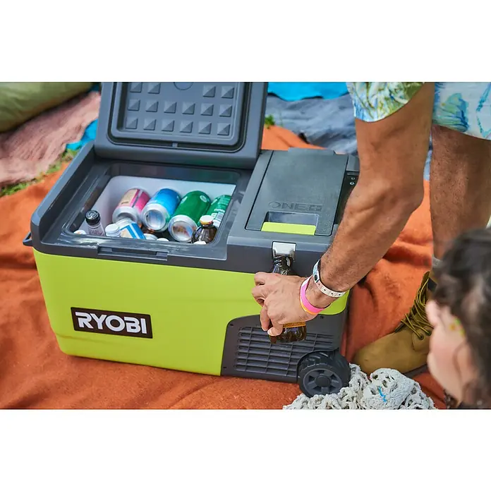 Ryobi ONE+ Akku-Kühlbox Hybrid RY18CB23A-0 - L x B x H: 72,5 x 42 x 49,5 cm, Fassungsvermögen: 23 l - Kühler von Ryobi mit Getränken, eine Person öffnet eine Flasche Bier. Der tragbare Kühler in Gelb und Grau ist ideal für unterwegs.