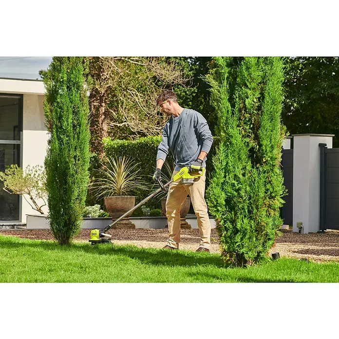 Ryobi ONE+ Akku-Rasentrimmer RY18LT33A - 18 V, Ohne Akku - Ein Mann, der mit einem Ryobi Rasentrimmer in einem gepflegten Garten arbeitet. Er trimmt das Gras fachmännisch um Zypressen herum.