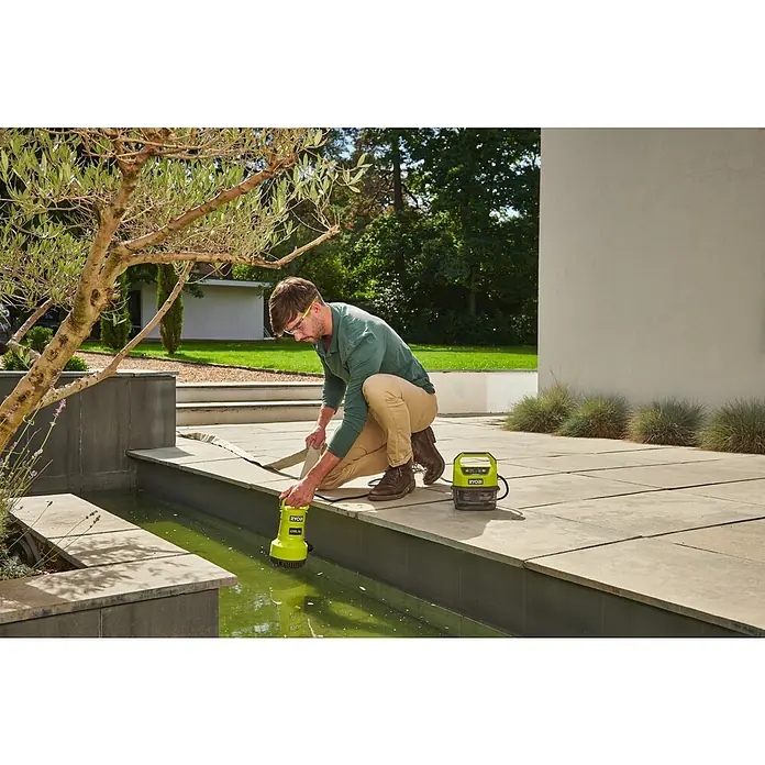 Ryobi ONE+ Schmutzwasserpumpe - Max. Fördermenge: 4.200 l/h - Ein Mann lässt eine gelbe RYOBI-Tauchpumpe in einen Teich ab, eine weitere Pumpe steht daneben.