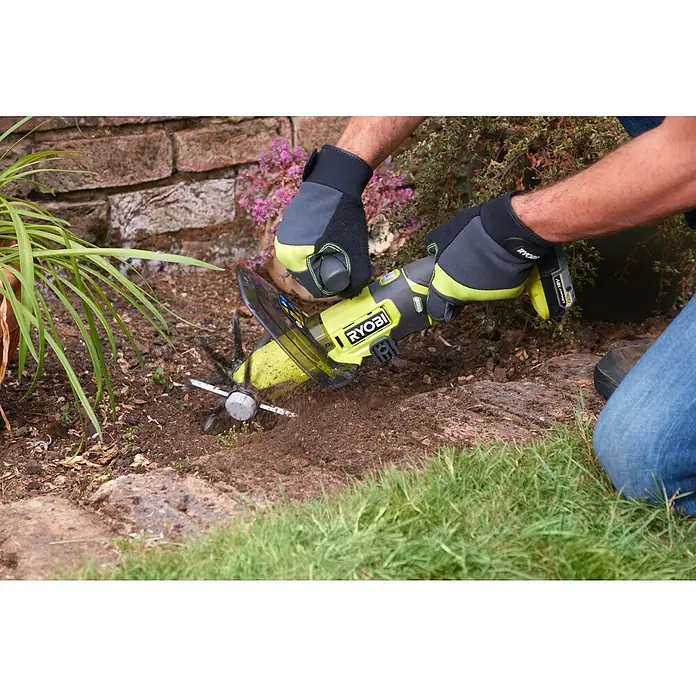 Ryobi ONE+ Akku-Bodenhacke RY18HCA-018 V, Ohne Akku - Nahaufnahme eines Akku-Kultivators von Ryobi in Aktion, der den Boden lockert, getragen von behandschuhten Händen.