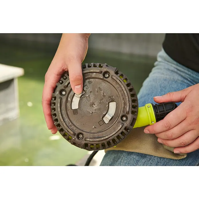 Ryobi ONE+ Schmutzwasserpumpe - Max. Fördermenge: 4.200 l/h - Nahaufnahme einer Person, die ein rundes, graues Gerät mit Drehverschlüssen vor einem unscharfen Hintergrund hält.
