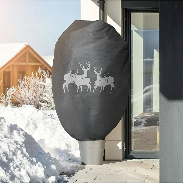 Windhager Abdeckhaube Protect - Hirsch, XXL, L x B: 1,4 x 2 m, Grau - Pflanztopf mit Winterschutzhülle, dunkelgrau mit Hirschmotiv, steht draußen im Schnee neben einem modernen Haus.
