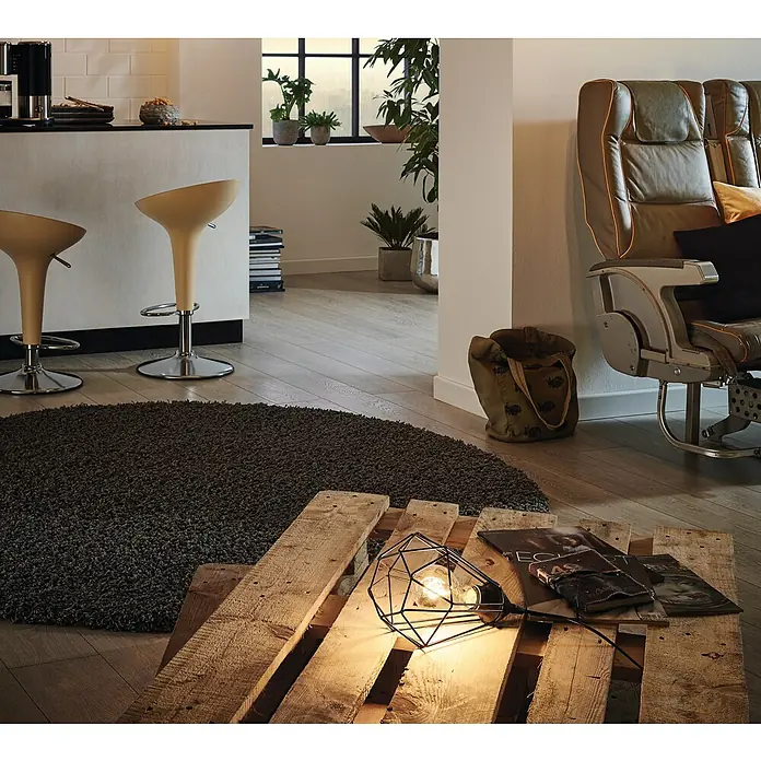 Eglo Tarbes Tischleuchte - 60 W, L x B x H: 26,5 x 26,5 x 17,5 cm, Schwarz, E27 - Eine moderne Inneneinrichtung mit einem ungewöhnlichen Lampendesign auf einer Holzpalette und einem runden, grauen Teppich.
