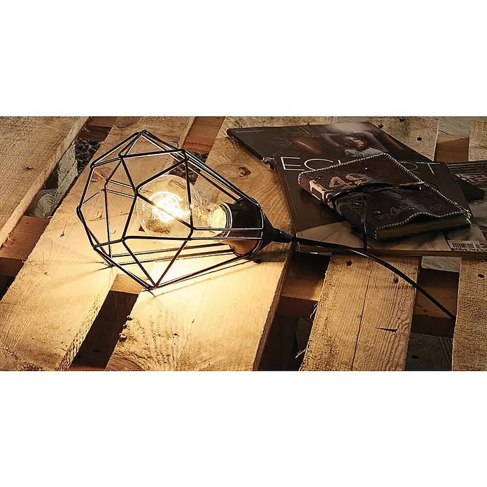 Eglo Tarbes Tischleuchte - 60 W, L x B x H: 26,5 x 26,5 x 17,5 cm, Schwarz, E27 - Diese Nahaufnahme zeigt eine moderne geometrische Lampe mit Glühbirne, die auf einer rustikalen Holzoberfläche steht. Buch und Zeitschrift liegen daneben.