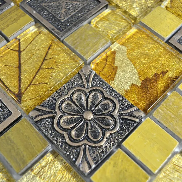 Mosaikfliese Crystal Mix XCM NIKO90 - 30 x 30 cm, Gold, Glänzend - Nahaufnahme eines Mosaiks mit goldenen, blattverzierten und metallischen Akzenten, das ein luxuriöses und dekoratives Element zeigt.