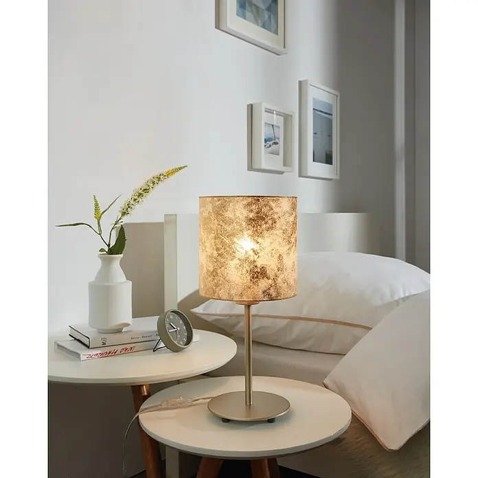 Eglo Viserbella Tischleuchte - 60 W, Champagner, E27 - Nahaufnahme einer eingeschalteten goldenen Tischleuchte mit Muster auf einem Nachttisch neben einem Bett.