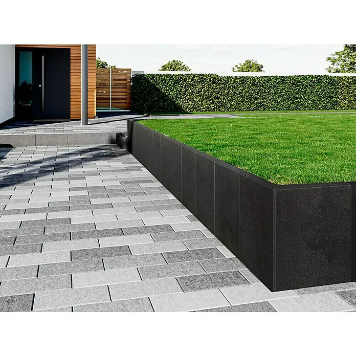 Diephaus L-Stein - 60 cm, 50 cm, Stärke: 7 cm, Anthrazit - Pflastersteine aus Beton und eine Rasenfläche, die durch eine schwarze Steinmauer abgegrenzt wird.
