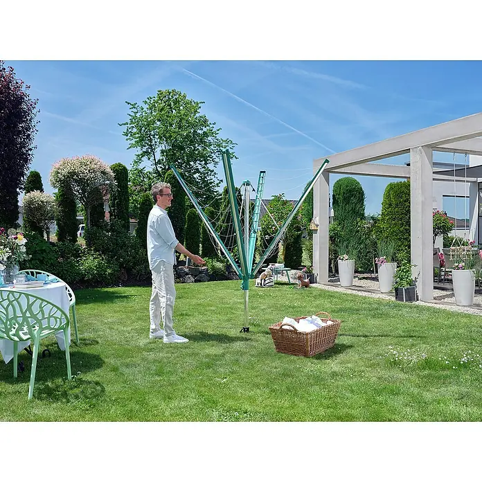 Leifheit Wäschespinne Linomatic 500 Deluxe Cover - Länge Wäscheleine: 50 m, Geeignet für Anzahl Waschmaschinenfüllungen: 5 Stk. - Ein Mann steht neben einem Wäscheständer im Garten. Ein Wäschekorb steht auch im Gras.