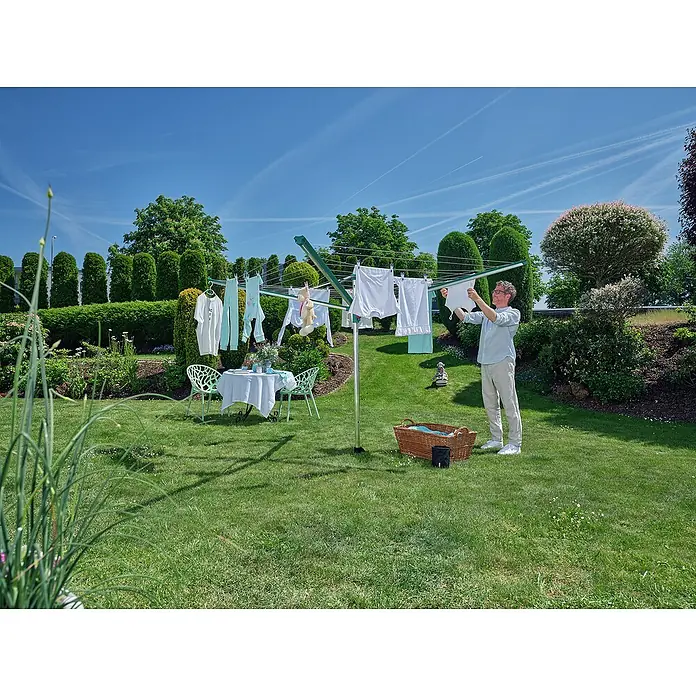 Leifheit Wäschespinne Linomatic 500 Deluxe Cover - Länge Wäscheleine: 50 m, Geeignet für Anzahl Waschmaschinenfüllungen: 5 Stk. - Ein Wäscheständer im Garten, beladen mit frisch gewaschener Kleidung, während ein Mann ein Wäschestück aufhängt.