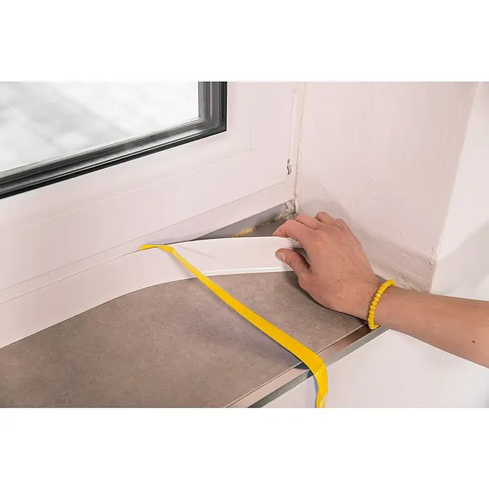 Schellenberg Flachleiste - 1,5 m x 40 mm x 2,5 mm, Weiß - Ein Mann montiert eine weiße Fensterbank unter einem Fenster, um die Installation abzuschließen, wobei er gelbes Klebeband verwendet.