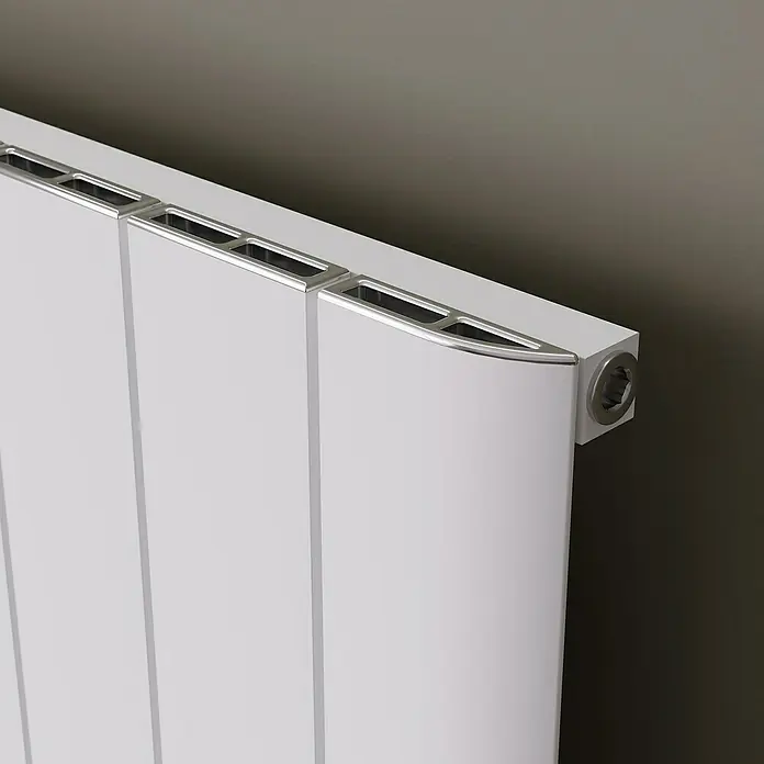 Ximax Designheizkörper Trigo - B x H: 470 x 1.800 mm, Wärmeleistung bei Vorlauftemperatur von 75 °C (D: 50): 960 W, Weiß - Nahaufnahme eines weißen Heizkörpers mit silberfarbenen Akzenten an der Oberseite. Das Heizgerät steht vor einer dunklen Wand.