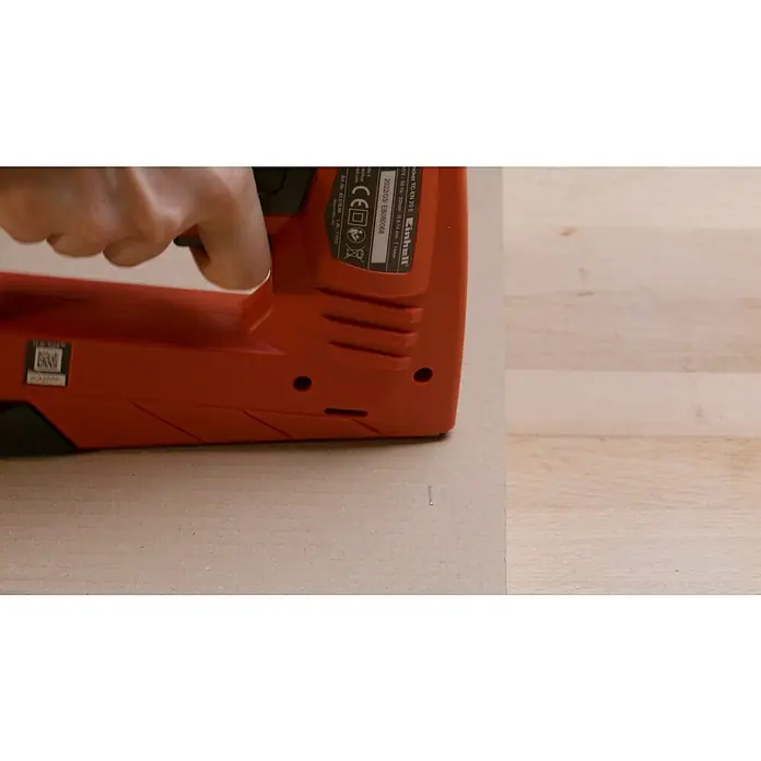 Einhell Elektrotacker - Klammertiefe: 6 mm - 14 mm - Nahaufnahme eines roten Einhell TC-EN 20 E Elektrotackers, der auf einer hellen Holzoberfläche platziert ist und von einer Hand bedient wird.