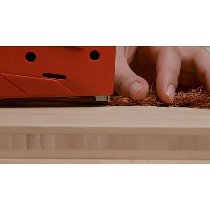 Einhell Elektrotacker - Klammertiefe: 6 mm - 14 mm - Nahaufnahme eines roten Kantenanleimgeräts, das auf einer Holzplatte mit einer Hand in der Nähe bedient wird.