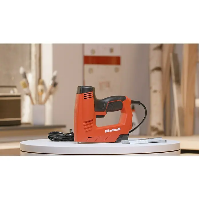 Einhell Elektrotacker - Klammertiefe: 6 mm - 14 mm - Nahaufnahme eines Einhell Elektrotackers auf einer weißen Oberfläche, zusammen mit dazugehörigen Heftklammern, präsentiert für Handwerks- und DIY-Projekte.
