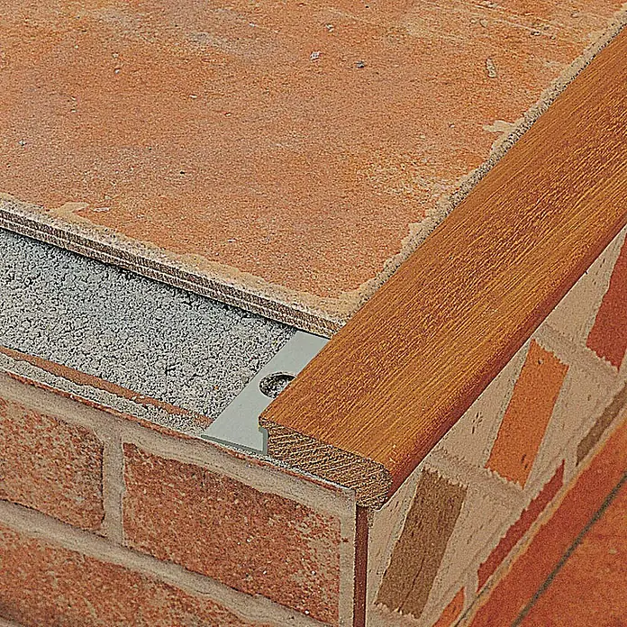 Perfil para baldosas para peldaño - Madera, Marrón, 2,5 m x 18 mm - Primer plano de un borde de escalera de madera, fijado sobre baldosas y ladrillo.