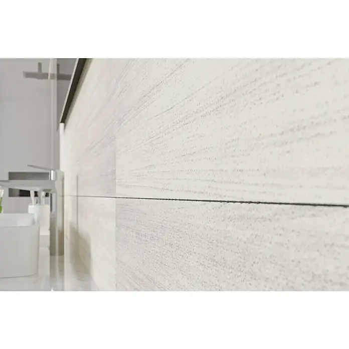 Wandfliese Layers Bone Base - 30 x 90 cm, Elfenbein, Matt - Nahaufnahme einer strukturierten, weißen Badezimmerwand mit minimalistischem Wasserhahn und Spülbecken, die ein modernes Design zeigt.