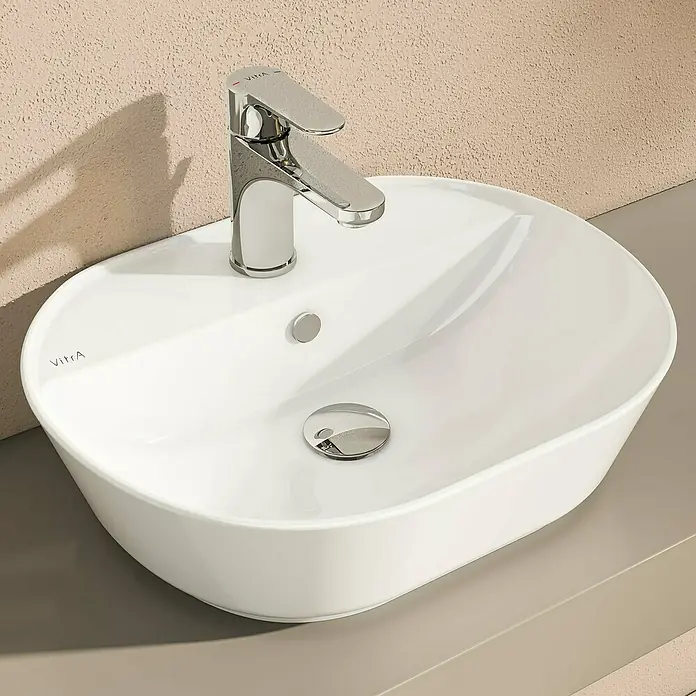 VitrA Aurinia 2.0 Aufsatzwaschbecken - 54,5 x 43 cm, Hahnloch: Mitte, Mit Überlauf, Weiß - Nahaufnahme eines eleganten, ovalen Waschbeckens mit einem modernen Chromhahn, das ein stilvolles Badezimmer-Ambiente ausstrahlt.