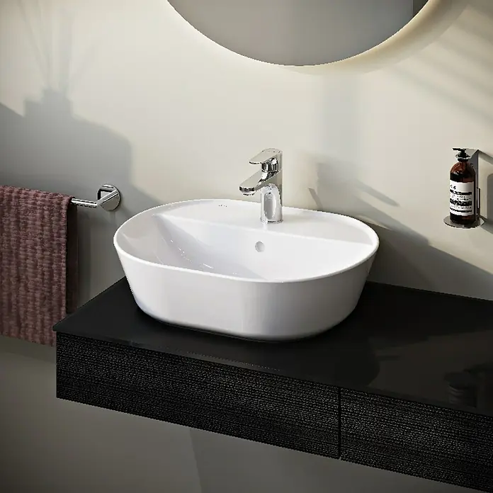 VitrA Aurinia 2.0 Aufsatzwaschbecken - 54,5 x 43 cm, Hahnloch: Mitte, Mit Überlauf, Weiß - Elegantes Waschbecken-Design: Ein ovales, weißes Aufsatzwaschbecken mit Armatur auf einer schwarzen Waschtischplatte unter einem runden Spiegel.