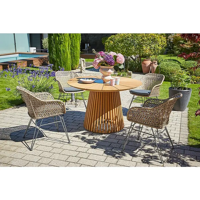 Sunfun Gartenmöbel-Set Osby/Maja - 5 -tlg., Teak/Aluminium/Stahl/PE-Geflecht, Teak/Braun/Grau - Ein runder Holztisch mit vier Korbstühlen und silbernen Beinen steht auf einer Terrasse. Der Tisch ist mit Blumen und Geschirr dekoriert.