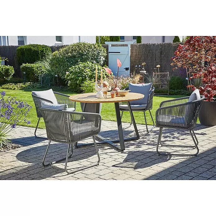 Sunfun Carina Gartentisch rund - Ø x H: 115 x 76 cm, Akazienholz, Teak - Outdoor-Essgruppe mit dunkelgrauen Geflechtstühlen, hellen Kissen und Holztisch mit dunkelgrauen Beinen auf einer Terrasse.
