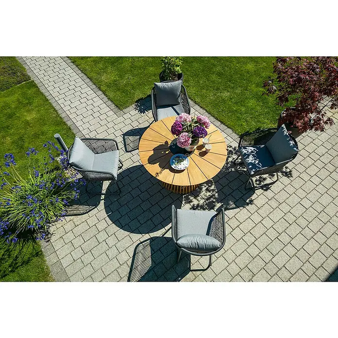 Sunfun Gartenmöbel-Set Osby/Maja - 5 -tlg., Teak/Aluminium/Stahl/Kunststofffaser-Strings, Teak/Grau - Gartenset mit rundem Tisch und vier Stühlen mit grauen Kissen auf einer gepflasterten Terrasse mit Blumen und Grün.