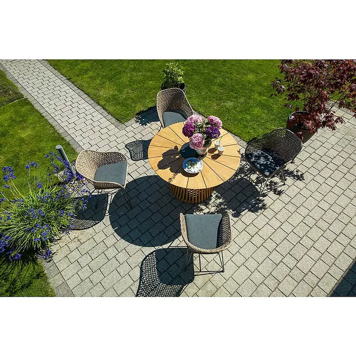 Sunfun Gartenmöbel-Set Osby/Maja - 5 -tlg., Teak/Aluminium/Stahl/PE-Geflecht, Teak/Braun/Grau - Gartenmöbel-Set mit rundem Holztisch und vier Korbstühlen mit grauen Kissen auf einer Steinterrasse, umgeben von Grünflächen und Pflanzen.