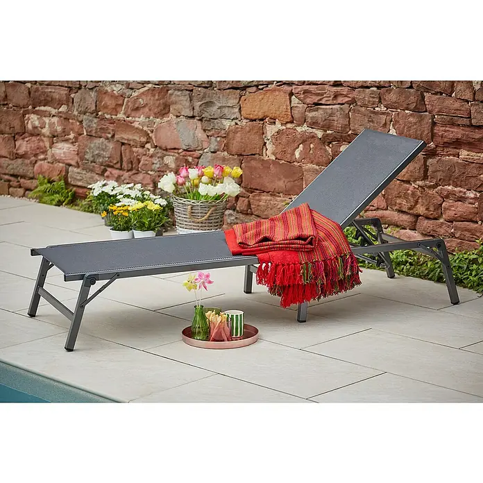 Sunfun Maja Gartenliege - B x T: 63 x 186 cm, Anthrazit, Stahl, Klappbar - Graue Sonnenliege aus Stoff mit einer roten Decke und einem Beistelltisch mit Getränken und Blumen auf einer Terrasse mit Blumen.