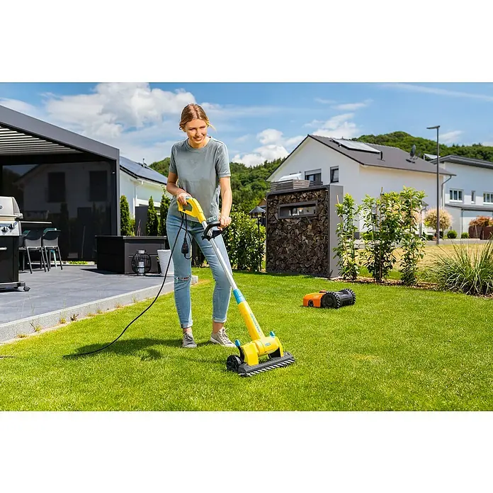 Gloria MultiBrush Grasscherenaufsatz FineCutPassend für: MultiBrush PLUS Geräte - Eine Frau benutzt einen gelben Rasenlüfter auf einem grünen Rasen, während ein Rasenmähroboter im Hintergrund steht.