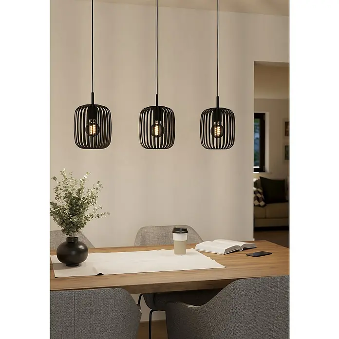 Eglo Romazzina Pendelleuchte - 40 W, L x B x H: 90 x 20 x 11 cm, Schwarz, E27 - Drei moderne, schwarze Pendelleuchten mit dekorativen Glühbirnen hängen über einem Esstisch, der mit einer Vase und einem Buch dekoriert ist.