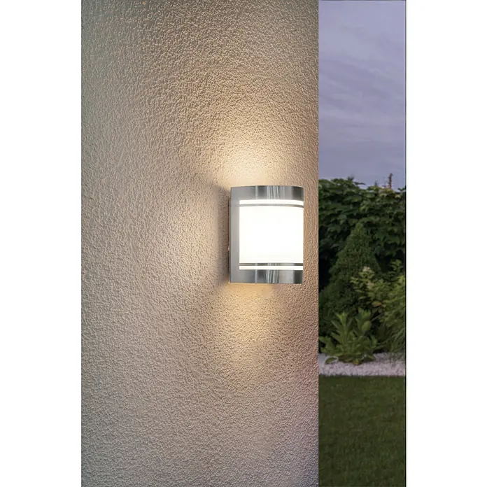 Außenwandleuchte - 40 W, 140 x 105 x 165 mm, Weiß, IP44 - Nahaufnahme einer modernen Außenwandleuchte mit silbernem Gehäuse und Milchglasscheibe, die ein warmes Licht an eine strukturierte Wand wirft.
