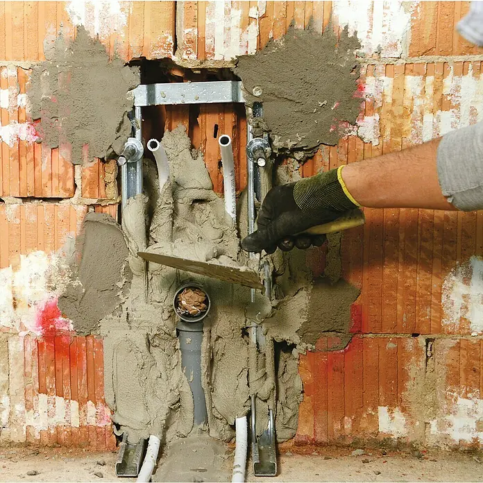 Kerakoll Mortero de reparación rápida Prestocem Eco - 5 kg - Un manitas utiliza una llana para aplicar mortero a un sistema de fontanería recién instalado dentro de una pared de ladrillo.