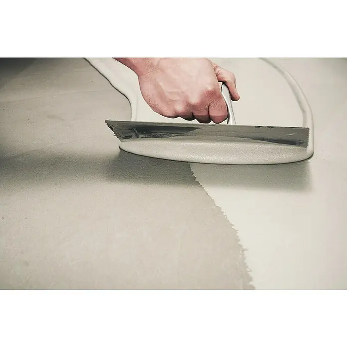 Kerakoll Membrana flexible impermeable Nanoflex Sin Límites - 20 kg, Espesor: 1 mm - 2 mm - Un artesano utiliza una llana para alisar un compuesto autonivelante para pisos de color claro sobre una superficie gris.