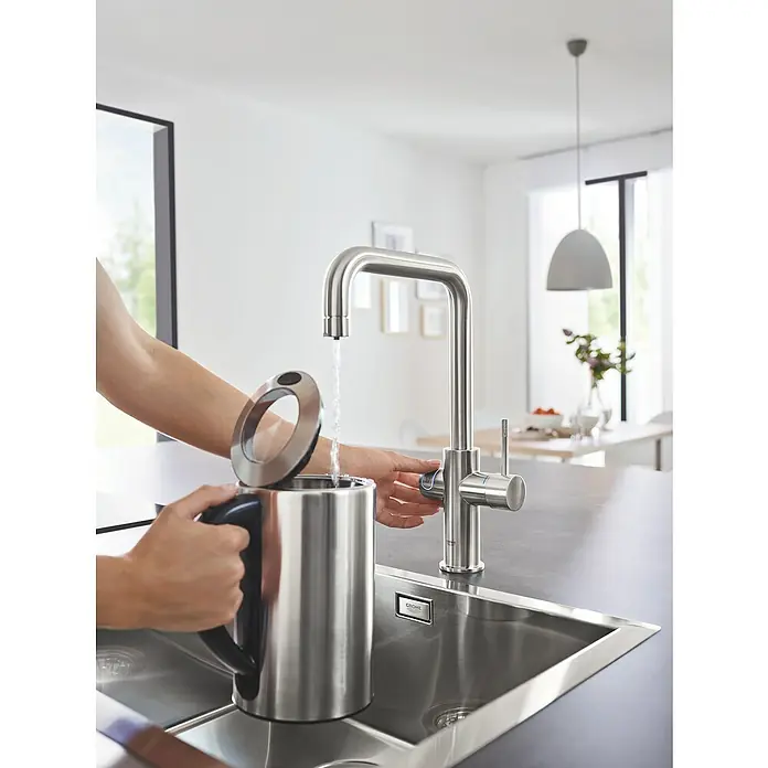 Grohe Spültischarmatur Blue Home - Höhe: 37,3 cm, U-Auslauf, Supersteel, Matt, Schwenkbar - Eine Person befüllt einen Wasserkocher mit einem GROHE Küchenarmatur in einer modernen Küche.