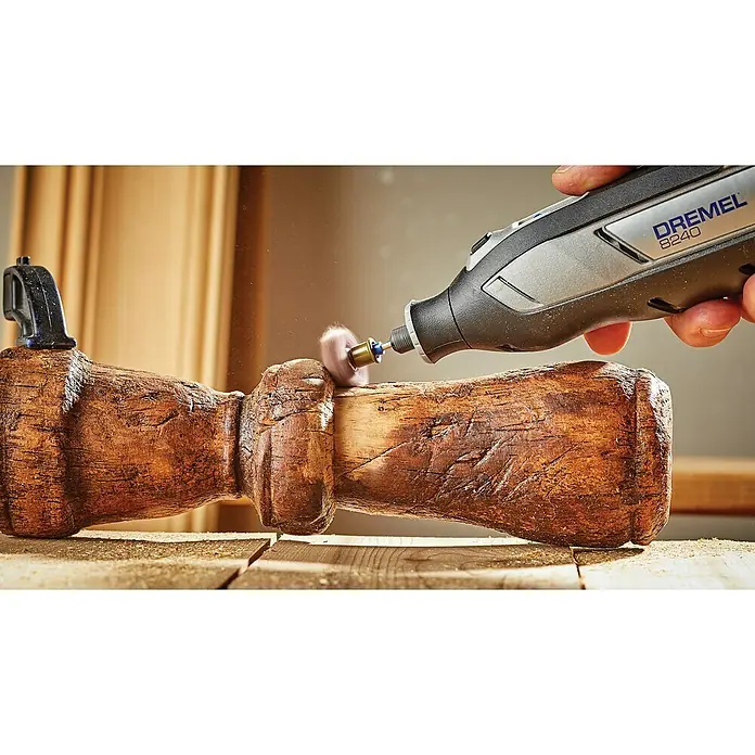 Dremel Akku-Multifunktionswerkzeug 8240-3/45 - 12 V, 1 Akku, 2 Ah, Inkl. 3 Aufsätzen und 45 Zubehören - Nahaufnahme eines Dremel 8240-Rotationswerkzeugs beim Schleifen eines Holzstücks, das mit einer Klemme auf einer Werkbank befestigt ist.
