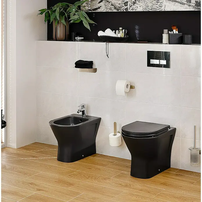 RAK Ceramics Feeling Stand-WC - Spülrandlos, Ohne Spezialglasur, Spülform: Tief, WC Abgang: Waagerecht, Schwarz - Badezimmeransicht mit schwarzem Bidet und Toilette, ergänzt durch moderne Armaturen und stilvolle Accessoires auf Fliesenboden.