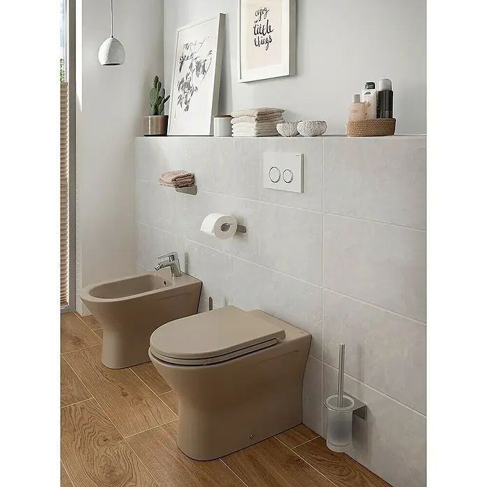 RAK Ceramics Feeling Stand-WC - Spülrandlos, Ohne Spezialglasur, Spülform: Tief, WC Abgang: Waagerecht, Cappuccino - Das Bild zeigt ein modernes Badezimmer mit einer beigen Toilette und einem Bidet auf einem Holzboden. Über der Toilette befindet sich ein Spülkasten.