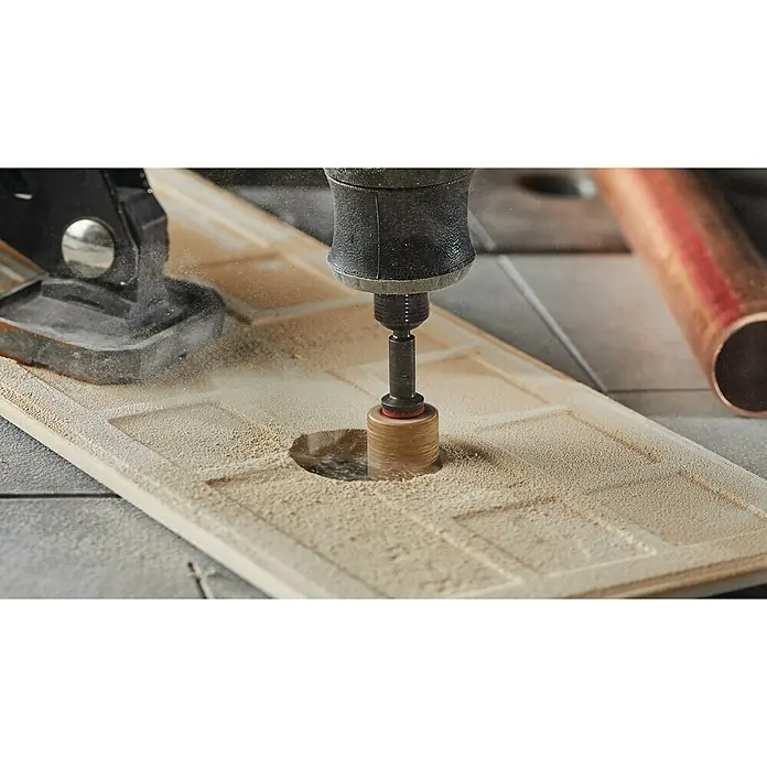 Dremel Schleifband / Lochbohrer 408DM (2-in-1) - Körnung: 60 - Das Bild zeigt eine Kernbohrmaschine, die ein Loch in eine helle Fliese bohrt, wobei der entstehende Staub deutlich sichtbar ist.