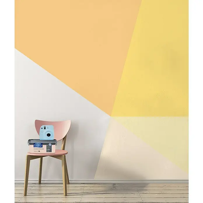 swingcolor Wandfarbe SIMPLY - Gelb - Nr. 28, 2,5 l - Die Innenfarbe SIMPLY in einem Eimer, zusammen mit einer Sofortbildkamera, auf einem Stuhl. Die Wand ist mit geometrischen Mustern in Gelb und Weiß bemalt.