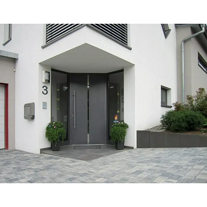 Diephaus L-Stein - 80 cm, 50 cm, Stärke: 7 cm, Anthrazit - Das moderne Wohngebäude präsentiert eine einladende Eingangstür mit Glaselementen, flankiert von üppigen Pflanzenarrangements und der Hausnummer.