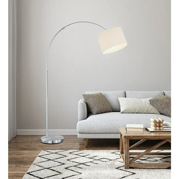 Trio Lighting Lámpara de pie Hotel - 60 W, Altura: 215 cm, Plateado, E27 - Lámpara de pie con base cromada curvada y pantalla cilíndrica, aportando un toque moderno al salón. La lámpara está al lado de un sofá gris.