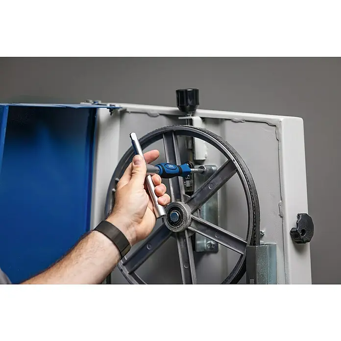 Scheppach Werkzeugkoffer TB170 - L x B x H: 40 x 31 x 10 cm, 135 -tlg. - Eine Person benutzt einen blauen Drehmomentschlüssel, um eine Schraube an einer Maschine festzuziehen, wobei der Fokus auf dem Werkzeug liegt.