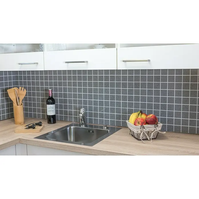 Mosaikfliese Quadrat Artifical XCM ASM43 - 30,5 x 30,5 cm, Grau, Glänzend - Eine Küchenspüle aus Edelstahl mit Armatur vor grauen Fliesen, umgeben von Küchenutensilien, einer Weinflasche und einem Obstkorb.