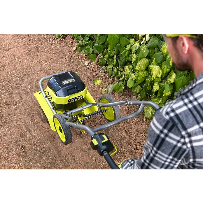 Ryobi Max Power Akku-Bodenhacke RY36CVXA-0 - Anzahl Akkus: Ohne Akku, Li-Ionen - Ein Mann benutzt eine gelbe Gartenfräse der Marke Ryobi, um den Boden vor einem Busch aufzulockern.