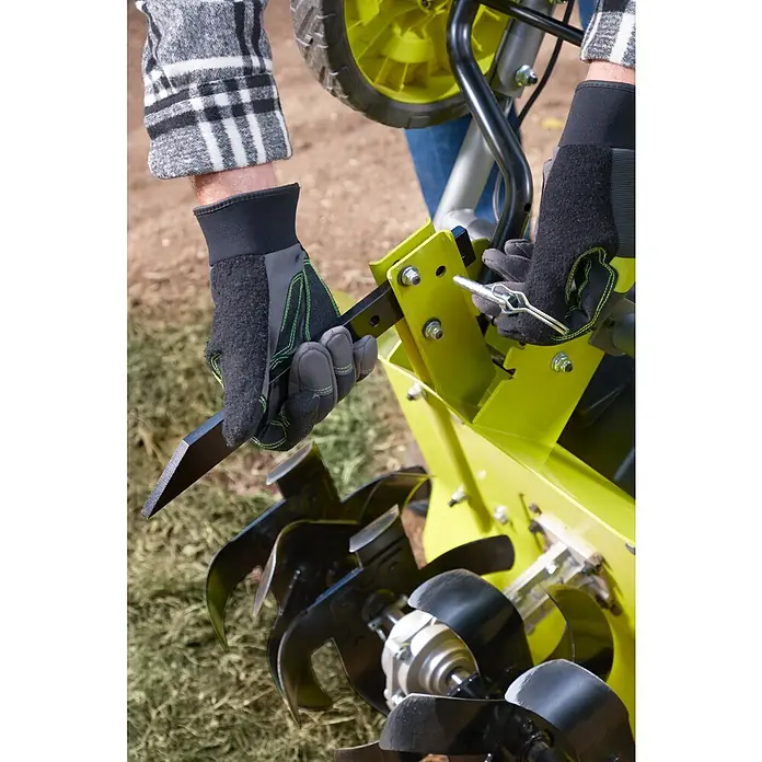 Ryobi Max Power Akku-Bodenhacke RY36CVXA-0 - Anzahl Akkus: Ohne Akku, Li-Ionen - Nahaufnahme eines Bedieners, der die Zinken an einem gelben RYOBI Kultivator/Bodenfräse einstellt und befestigt.