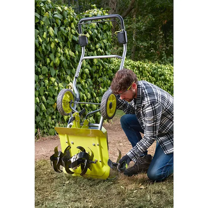 Ryobi Max Power Akku-Bodenhacke RY36CVXA-0 - Anzahl Akkus: Ohne Akku, Li-Ionen - Ein Mann inspiziert einen gelben Kultivator mit Rädern im Garten, umgeben von Grün. Er trägt Schutzbrille und Handschuhe.