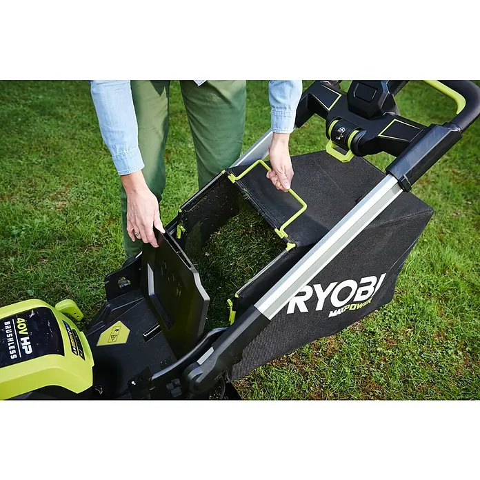 Ryobi Max Power Akku-Rasenmäher RY36LMXSP53A-160 - 36 V, 1 Akku, 6 Ah, Schnittbreite: 53 cm - Die Hände einer Person leeren Gras aus dem Grasfangsack eines Ryobi Max Power Rasenmähers auf einem Rasen.