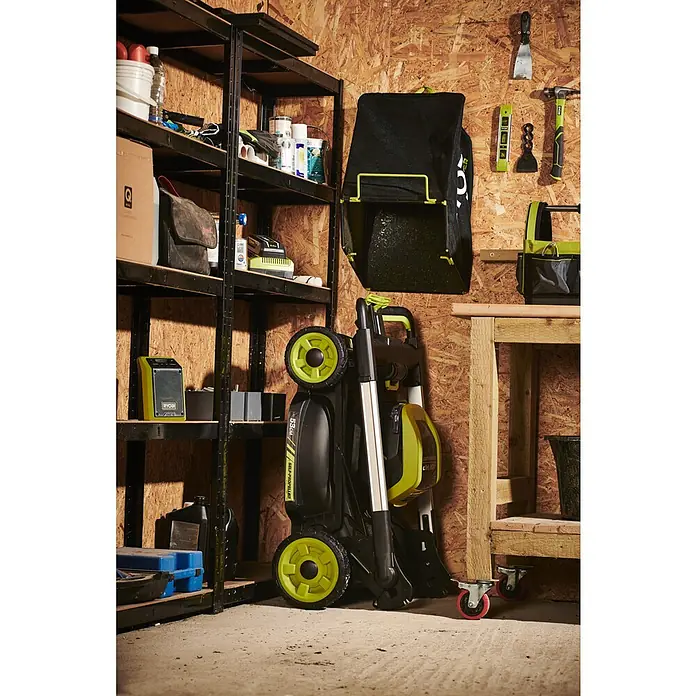 Ryobi Max Power Akku-Rasenmäher RY36LMXSP53A-160 - 36 V, 1 Akku, 6 Ah, Schnittbreite: 53 cm - Eine Ryobi Akku-Rasenmäher mit Fangkorb ist platzsparend an einer Werkstattwand gelagert. Praktische Werkzeuge hängen griffbereit daneben.
