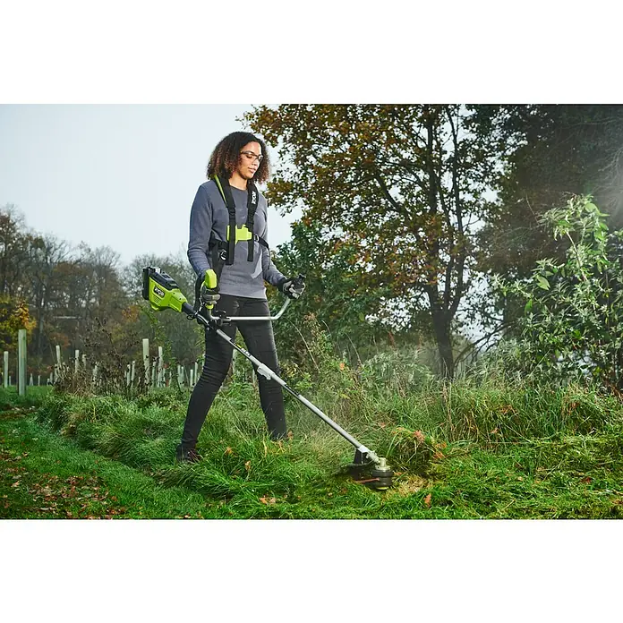 Ryobi Max Power Akku-Freischneider RY36BCX30A-9 - 36 V, Ohne Akku, Schnittbreite Faden: 40 cm, Schnittbreite Messer: 30 cm - Eine Frau benutzt eine Ryobi Akku-Motorsense im Freien. Der Trimmer ist mit einem Tragegurt für Komfort ausgestattet.